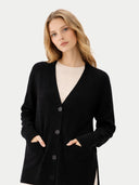 Woman wearing a black cardigan over a beige top on a light gray background.