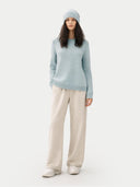 Woman wearing a light blue sweater and beige pants on a white background #color_cloud-blue