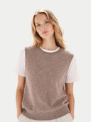 Close up of woman wearing a brown sleeveless sweater over a white shirt on a light background #color_taupe