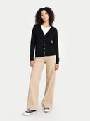 front view of a woman wearing a black v-neck cardigan, white shirt, beige pants, and black sneakers on a white background #color_black