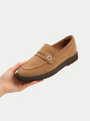 Brown loafer shoe held in a hand against a white background #color_almond