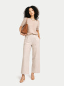 Woman wearing a beige top and pants with a brown handbag on a white background #color_beige