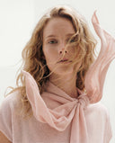 A woman with wind-blown hair in a pale pink cashmere top and a pink cashmere scarf knotted at the neck