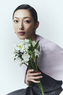 A woman in a lilac cashmere cardigan holding a bunch of white flowers, studio portrait
