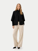Woman wearing a black coat and beige pants on a white background #color_taupe #color_dark-navy
