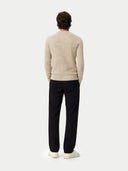 Back view of a man standing with a beige sweater and black pants on a white background #color_warm-grey