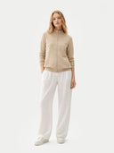 front view of a woman wearing a beige zip-up jacket and white pants on a white background #color_warm-grey