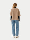 back view of a woman wearing a beige poncho jacket and blue jeans on a white background #color_taupe #color_dark-navy