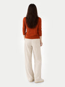 back view of a woman wearing a rust-colored sweater and beige pants on a white background #color_sugar-almond