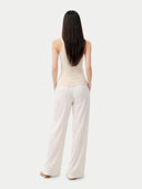 back view of Woman wearing a beige sleeveless top and white pants on a light gray background #color_off-white