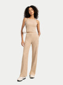 Woman wearing a beige knit top and pants with a white handbag on a light gray background #color_beige