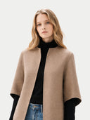 Woman wearing a beige cape over a black top and blue jeans on a white background #color_taupe #color_dark-navy