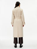 back view of a woman wearing a beige double breasted cashmere trench coat with belt  over a sweater and dark pants on a gray background #color_beige