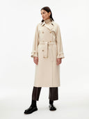 front view of a woman wearing a beige double breasted cashmere trench coat with belt  over a sweater and dark pants on a gray background #color_beige