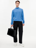 front view of A male model wearing a blue mock neck cashmere sweater and black pants, holding a handbag on a white background  #color_blue
