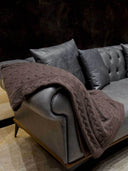 A brown cable knit blanket draped over a sofa.