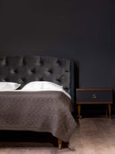 Dark luxury bedroom with a tufted black headboard, brown cable-knit blanket on the bed, and a modern wooden nightstand.