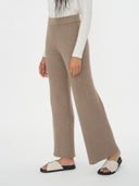 A pair of taupe-colored cashmere pants with a ribbed waistband, displayed on a model who is wearing a white long-sleeve top. #color_taupe