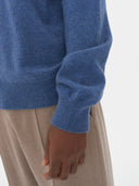 close up of a blue polo sweater sleeve and beige pants on a light gray background #color_bijou-blue