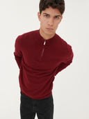 close up front view of a man wearing a red quarter cardigan and black jeans #color_bordeaux