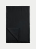 A black rectangular scarf with fringed edges, folded over in the bottom-left corner, displayed flat against a solid white background.